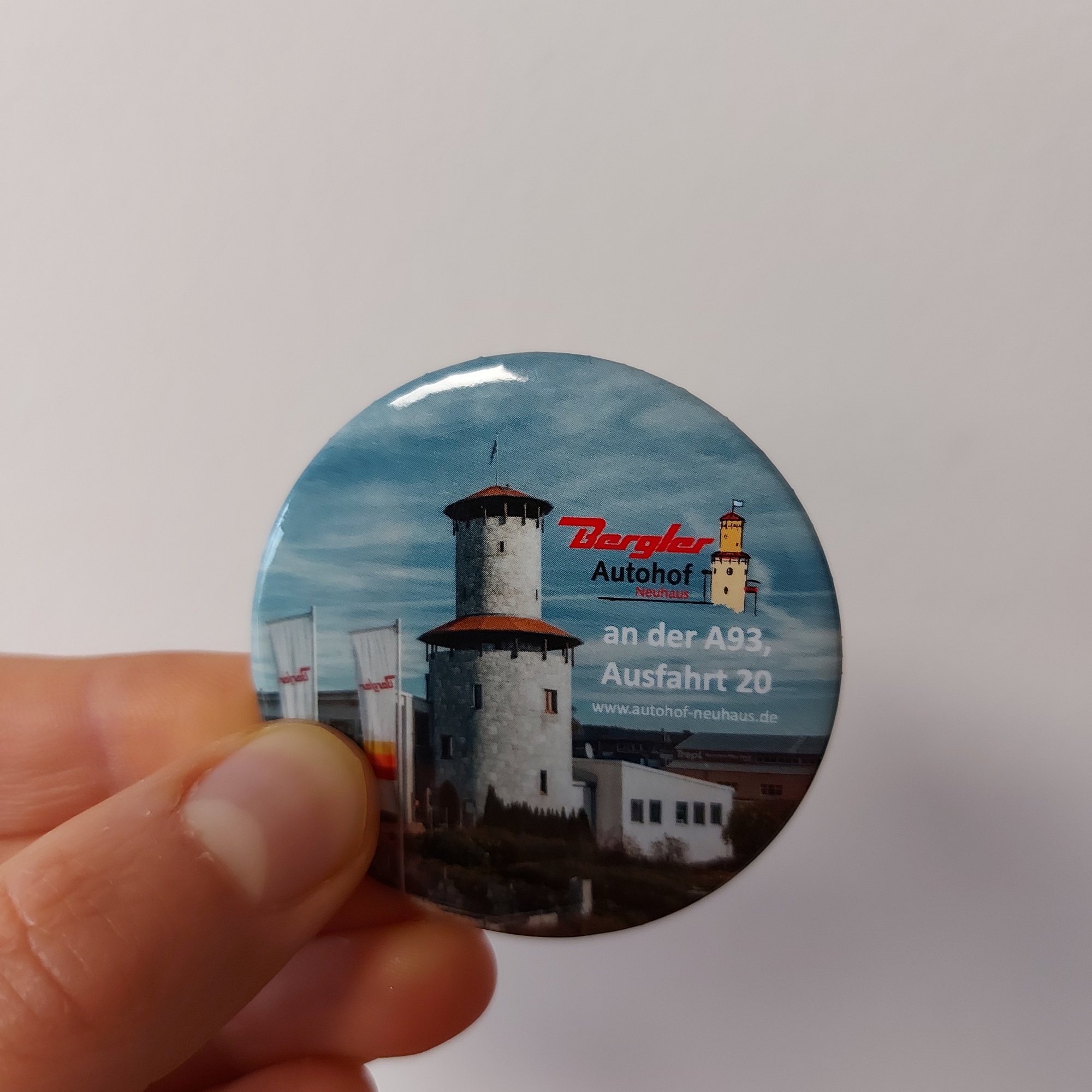 Ein runder Magnet wird in der Hand gehalten. Abgedruckt ist der markante Ritterturm, im Hintergrund strahlend blauer Himmel. Rechts im Bild das Autohof-Logo sowie die Internetseite.